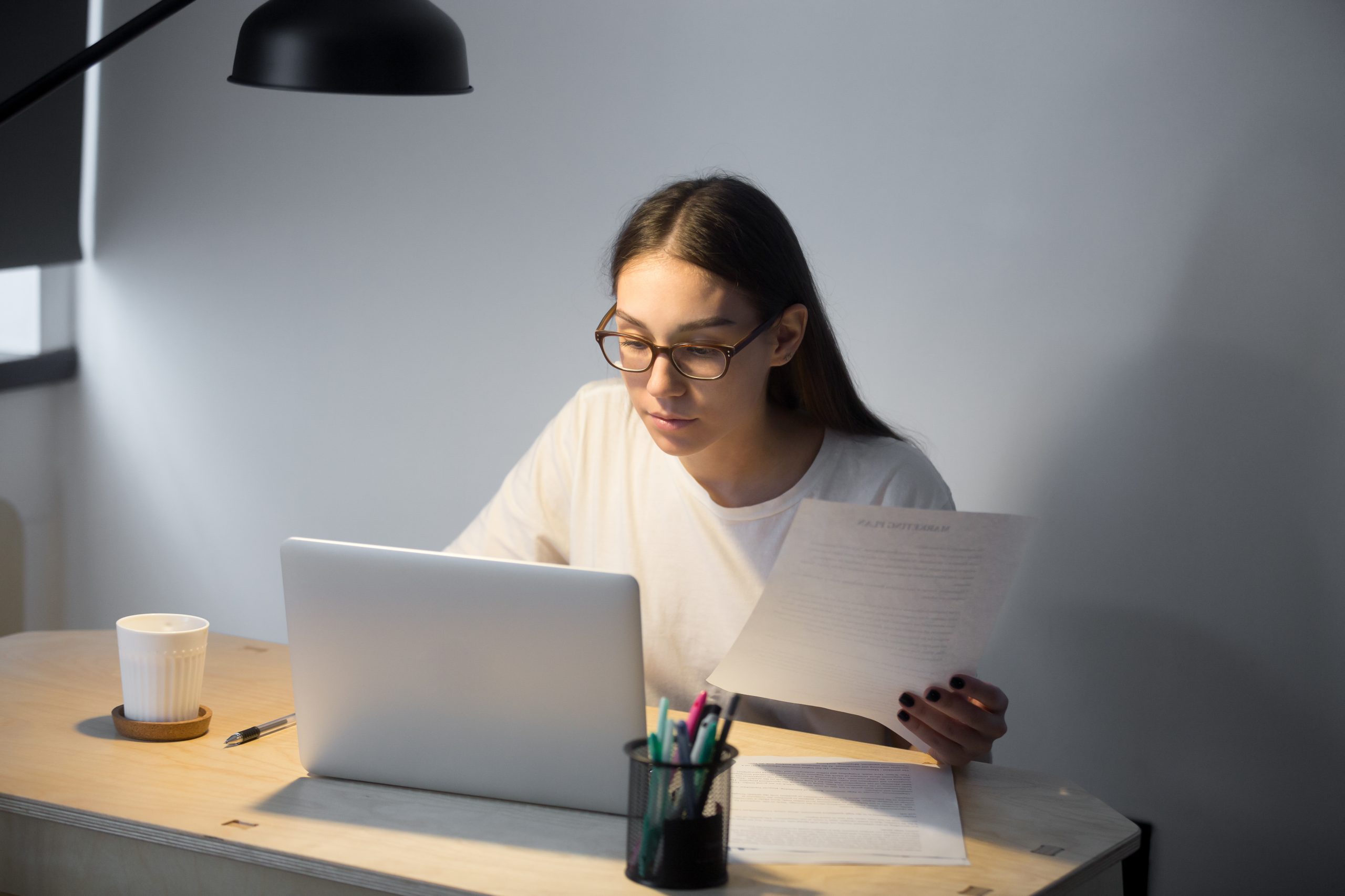 Millennial manager in glasses working on laptop and holding docu